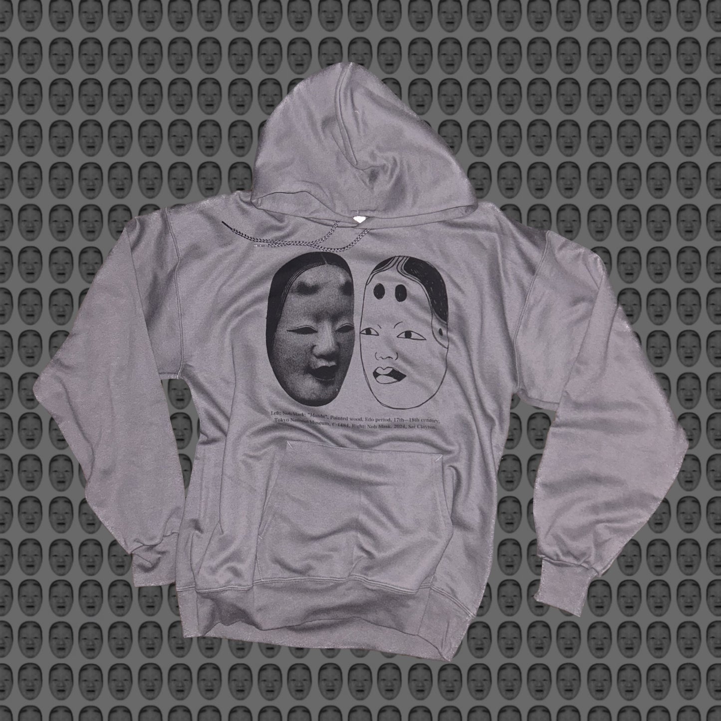 Gray hoodie with a face and noh mask design by STUDIO SAISAI on the front against a patterned background