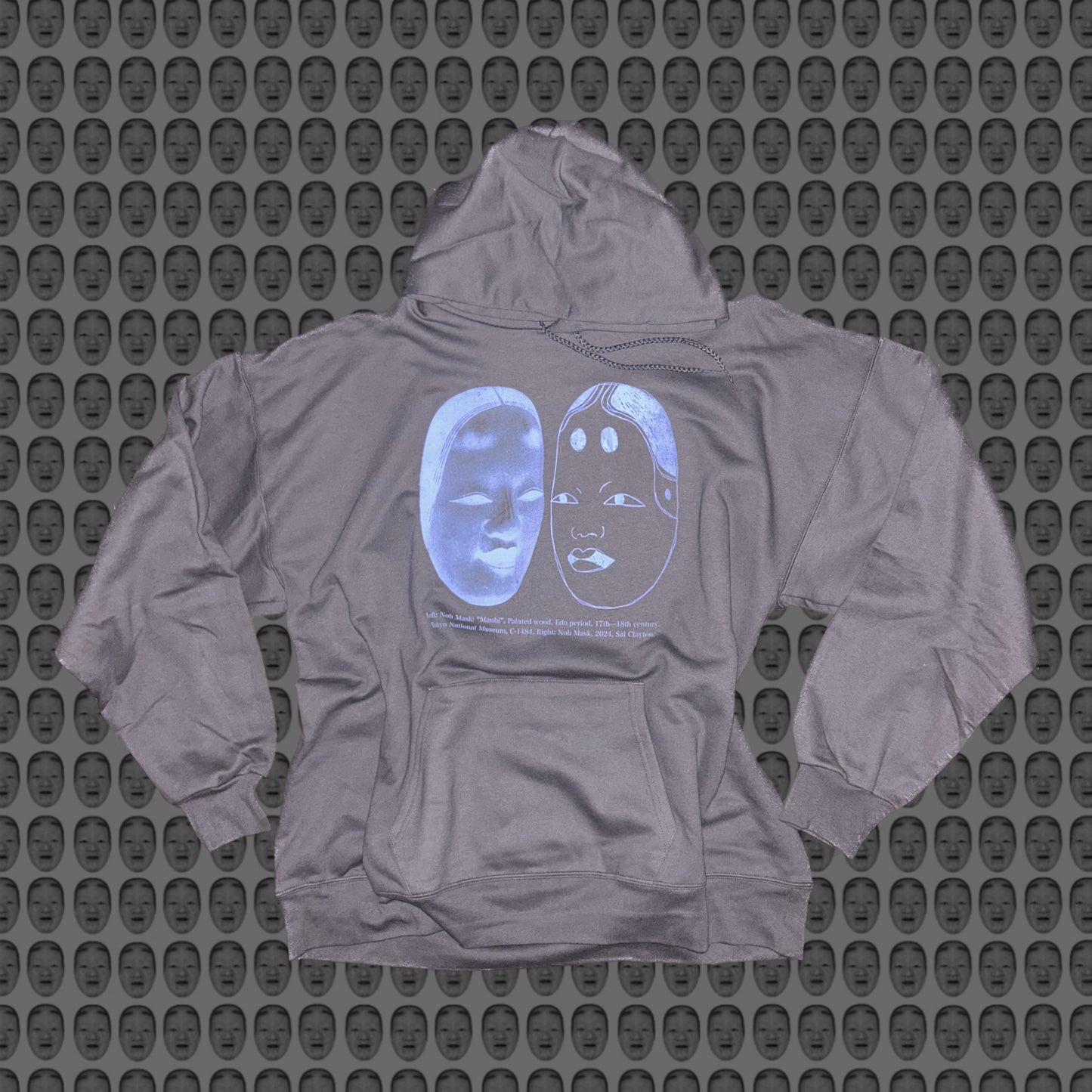 Gray hoodie with a blue face and noh mask design by STUDIO SAISAI on the front against a patterned background