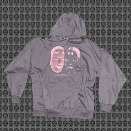 Gray hoodie with a pink face and noh mask design by STUDIO SAISAI on the front against a patterned background