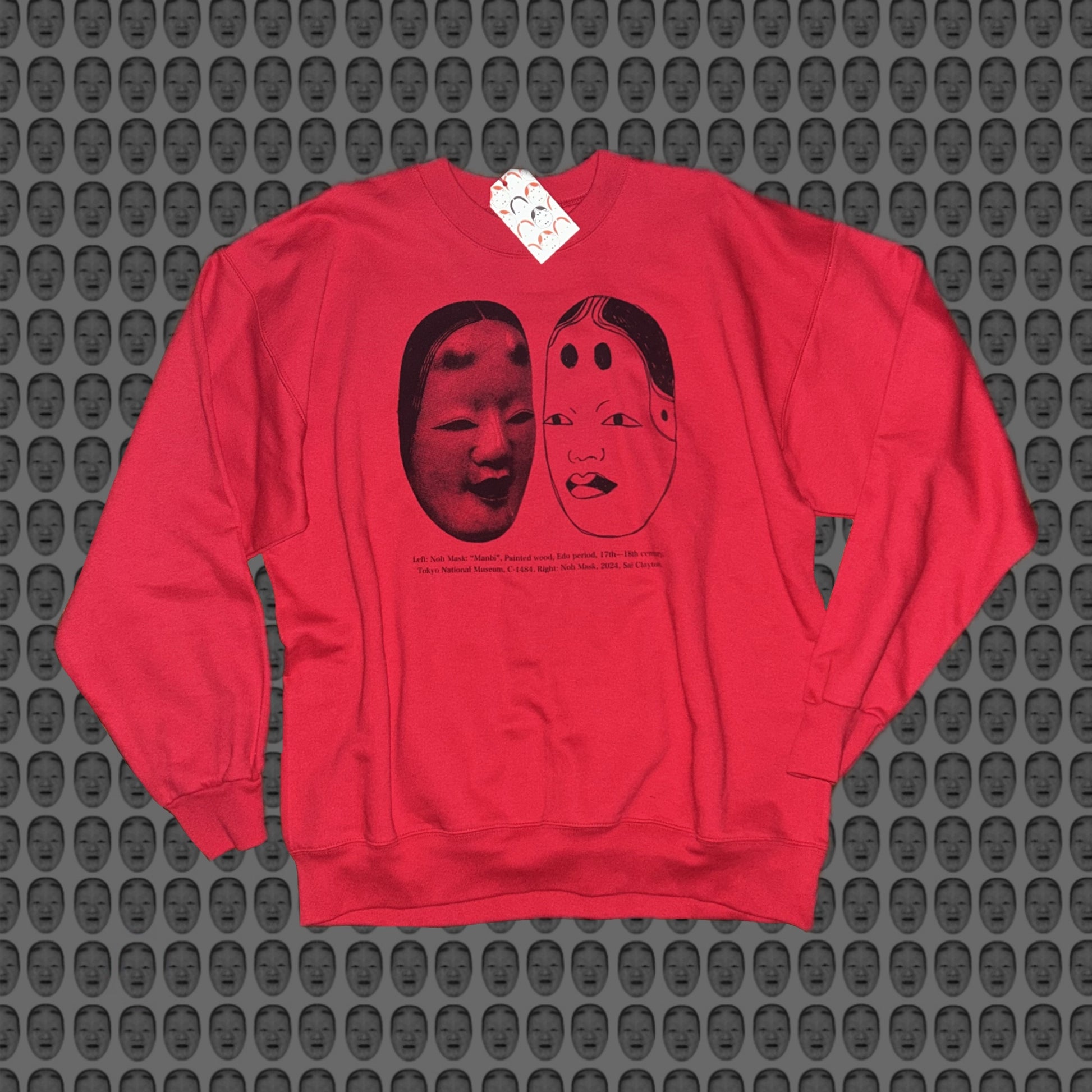 Red sweatshirt with a face and noh mask design by STUDIO SAISAI on the front against a patterned background