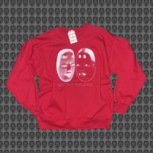 Red sweatshirt with a white face and noh mask design by STUDIO SAISAI on the front against a patterned background